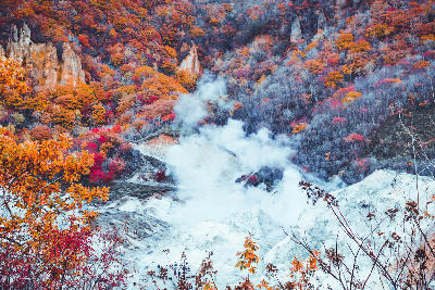 Steam rising from the mineral basin of Jigokudani Hell Valley surrounded by autumn foliage in Noboribetsu, Hokkaido, Japan.