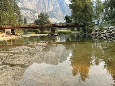 Sentinel Bridge reflected in the Merced River with shallow water and valley trees in Yosemite National Park.