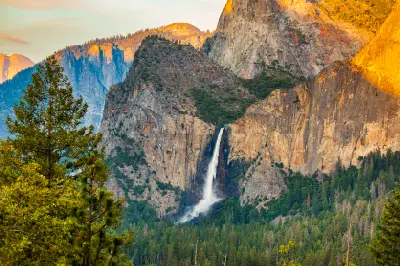 Bridalveil Fall Yosemite with tall waterfall dropping from granite cliffs above dense pine forest in warm afternoon light.