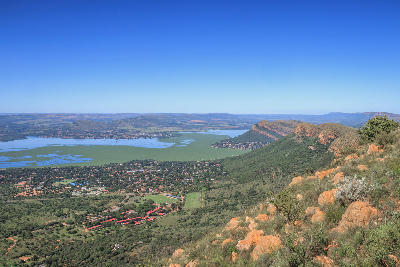 Panoramic view of Hartbeespoort Dam, surrounding valleys and the Magaliesberg mountain range from a mountainside viewpoint in North West Province, South Africa.