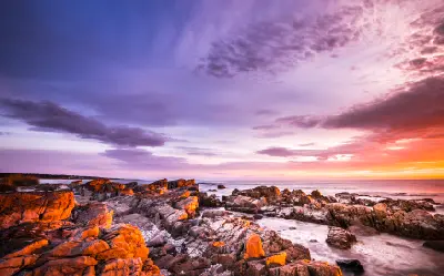Fiery sunrise over orange-lichen granite rocks and the ocean at the Bay of Fires, Tasmania.